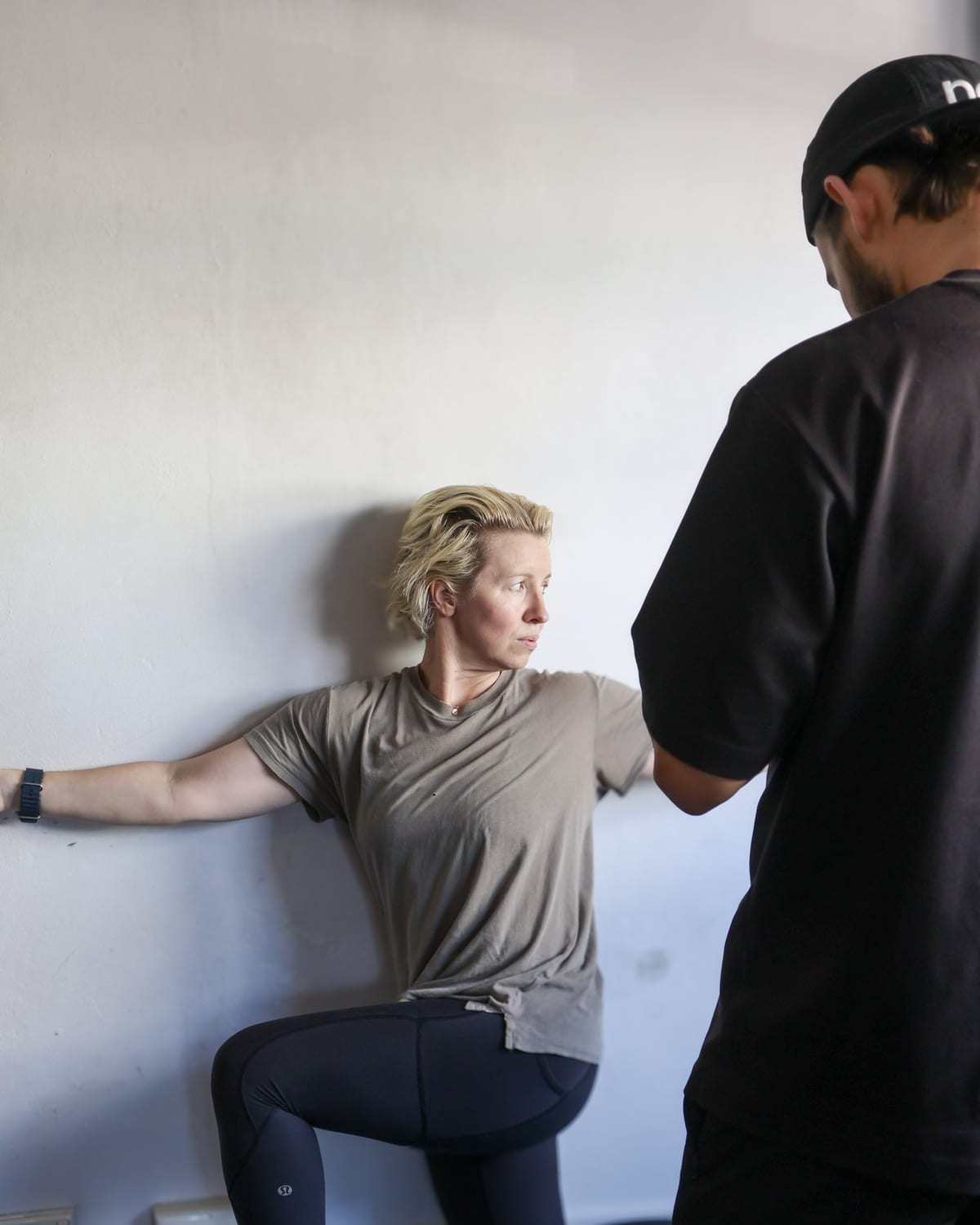 Chiropractor coaching a half-kneeling wall-supported hip exercise at SportsFit Five Dock