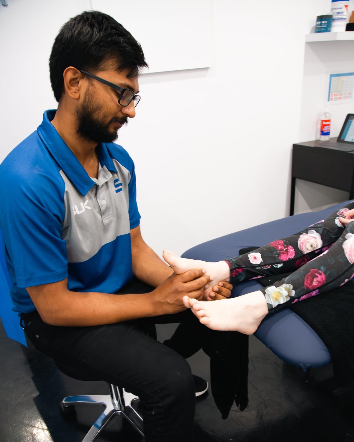 Physiotherapist seated, assessing a patient foot and ankle on the plinth at SportsFit Five Dock